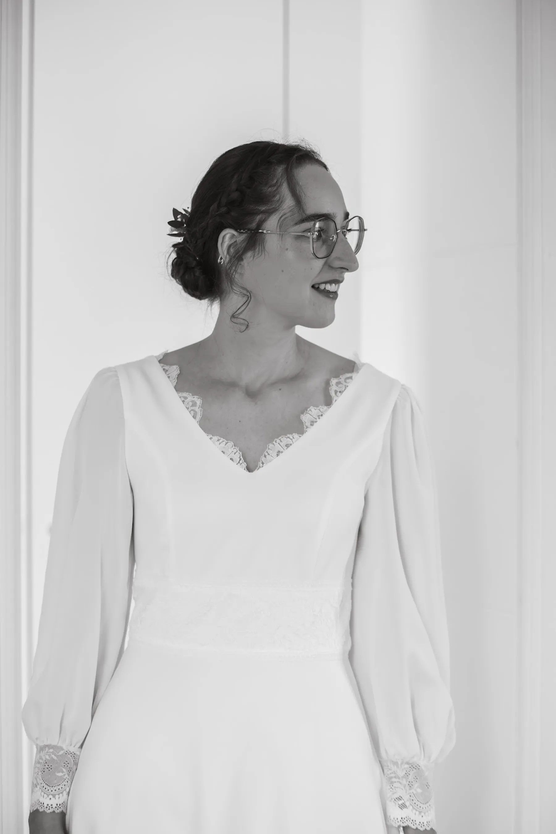 Portrait en noir et blanc d'Alice, robe de mariée à col V bordé de dentelle et poignets en dentelle, regard de côté