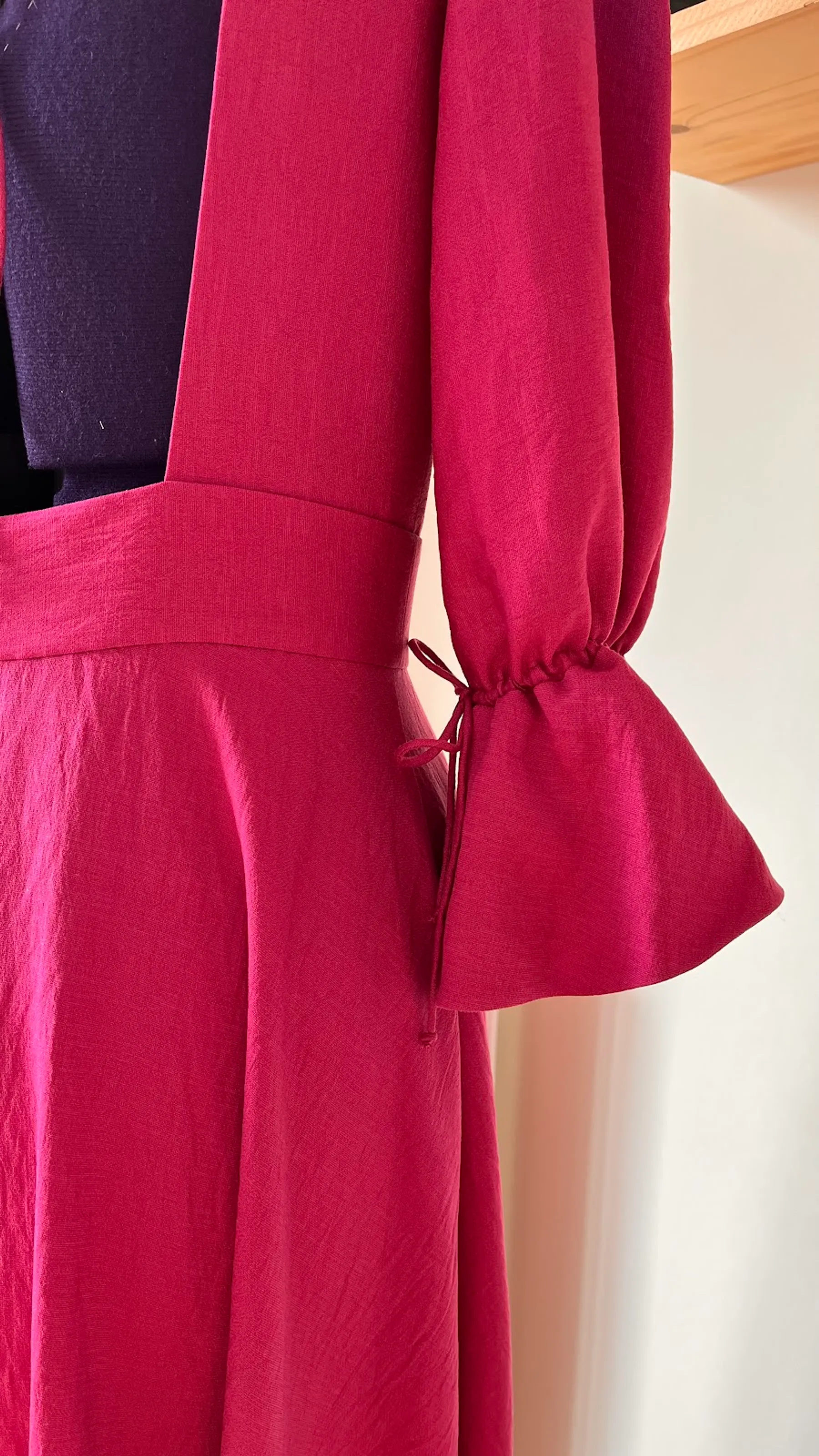 Détail de la manche à volant nouée d'un ruban et de la taille de la robe fuchsia