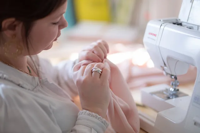 Hermine travaillant un tissu rose sous une machine à coudre.