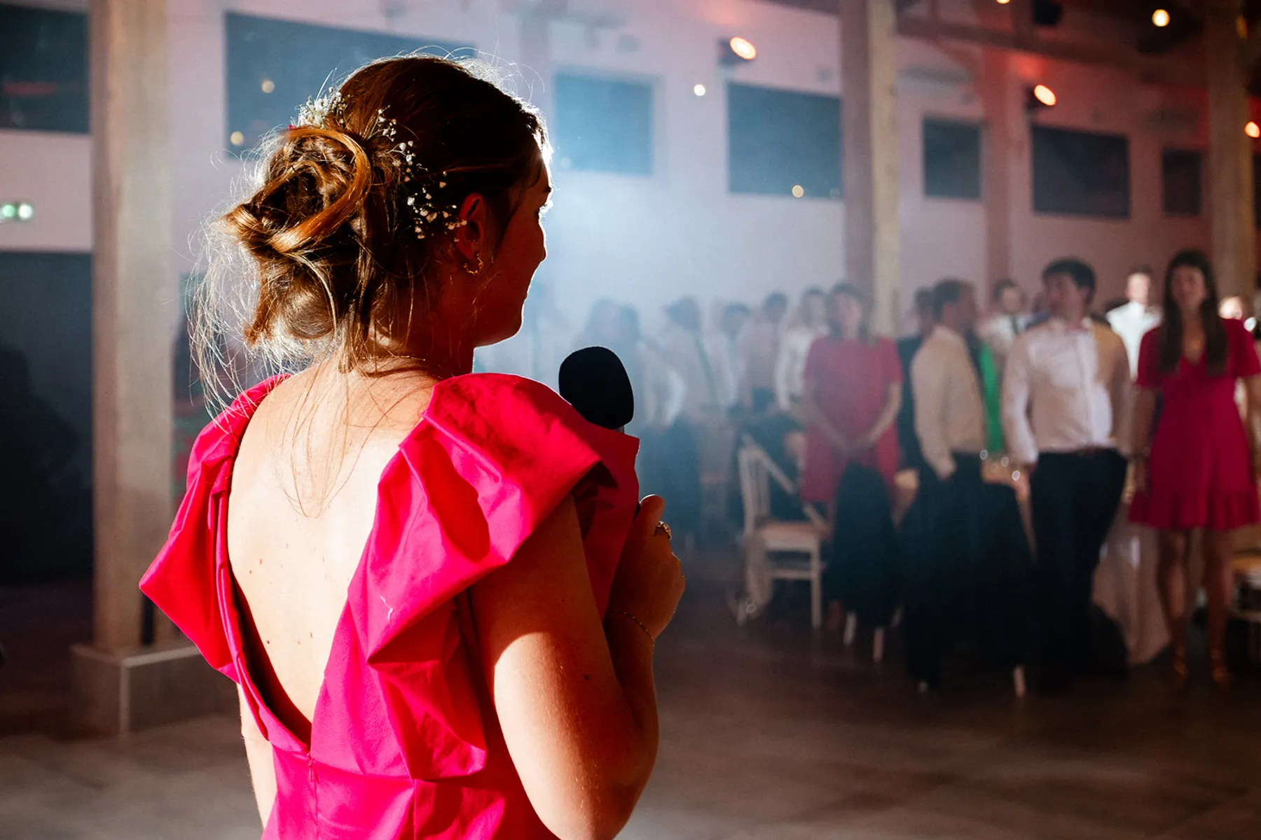 Mathilde de dos, micro à la main pour un discours, robe fuchsia au dos ouvert et épaules à volants