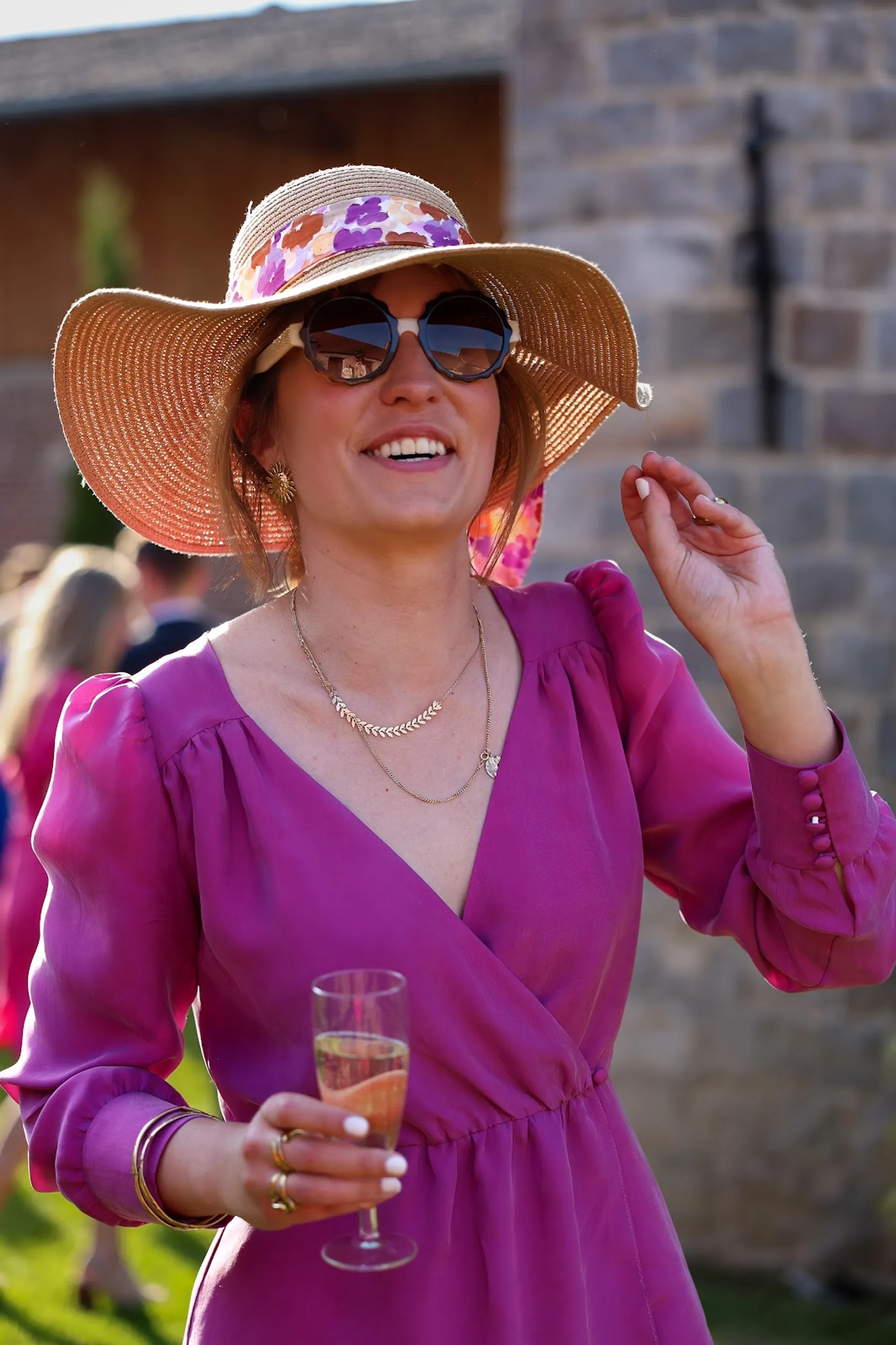 Pauline rit, coupe de champagne à la main, dans sa robe cache-cœur violette à manches longues et son chapeau à large bord